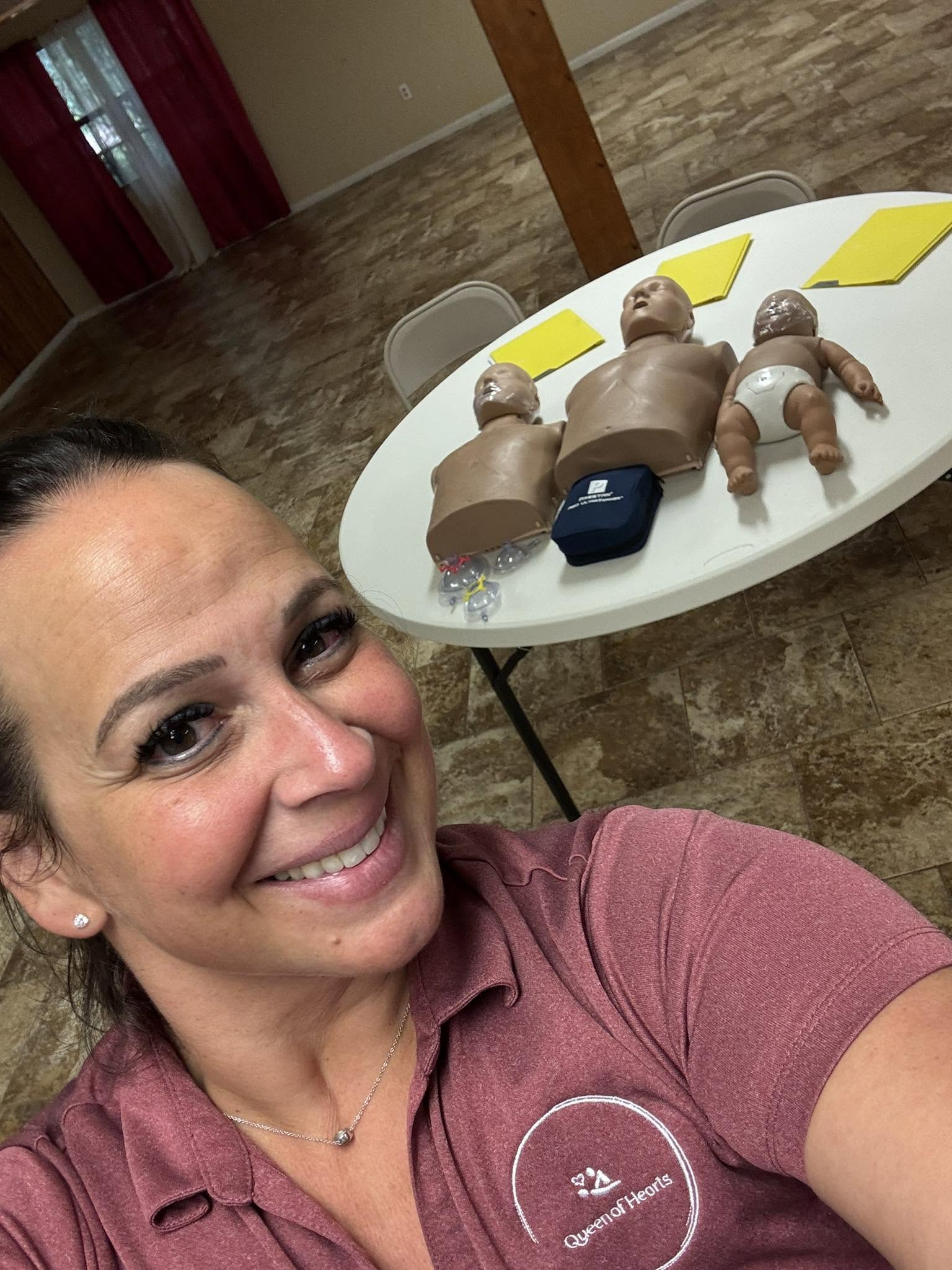 Rissa Johns smiling in her Queen of Hearts polo, with CPR training manikins set up on a table behind her